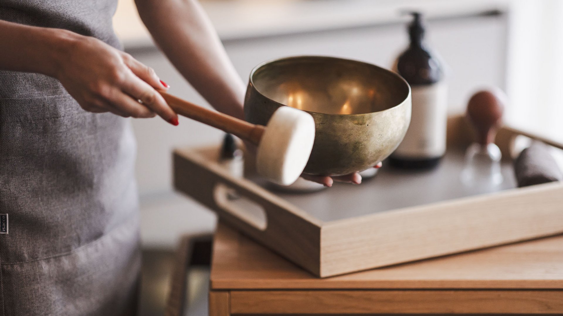 More than just a sauna in Val Pusteria/Pustertal: the Alpenreych Spa Person playing a singing bowl with a mallet in front of a wooden table with tray