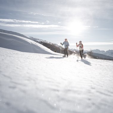 The best hotel at Plan de Corones/Kronplatz Two people snowshoeing on a snowy hill under bright sunlight
