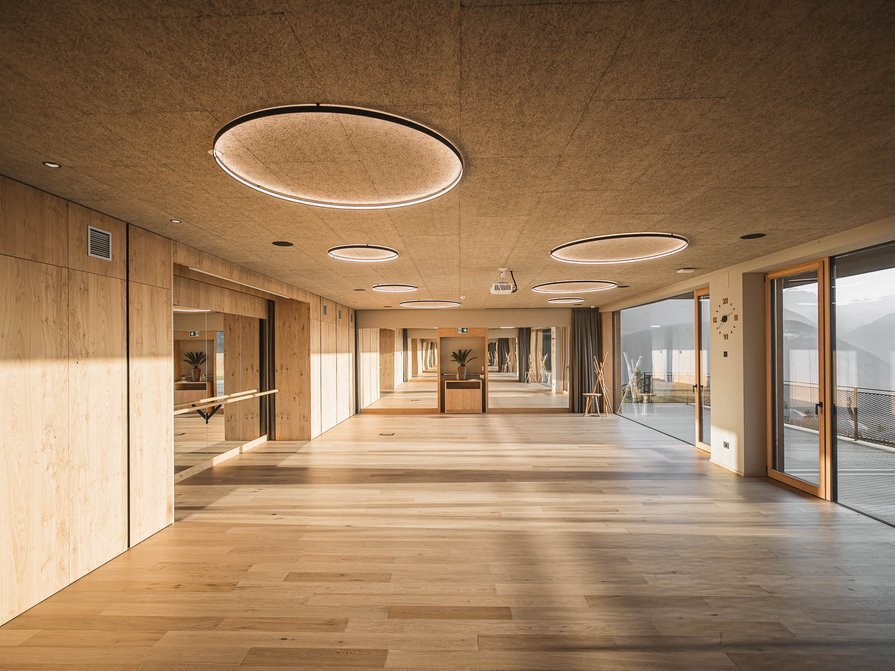 Unser Hotel in Olang zwischen Himmel und Erde Großer Raum mit Holzfußboden, Spiegelwand und großen Fenstern mit Bergblick
