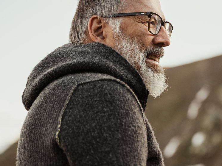 Atelier Moessmer Norbert Niederkofler Older man with glasses and gray sweater in front of mountain landscape