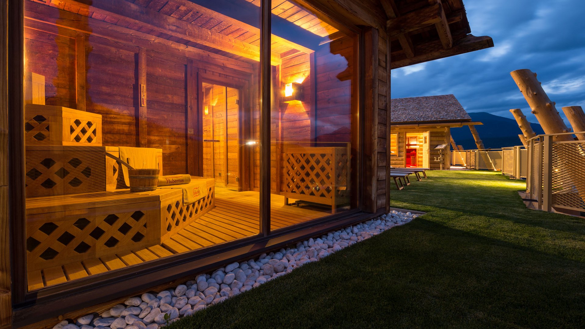 Our sauna, Plan de Corones/Kronplatz in full view Lit wooden sauna with glass wall and outdoor area at dusk