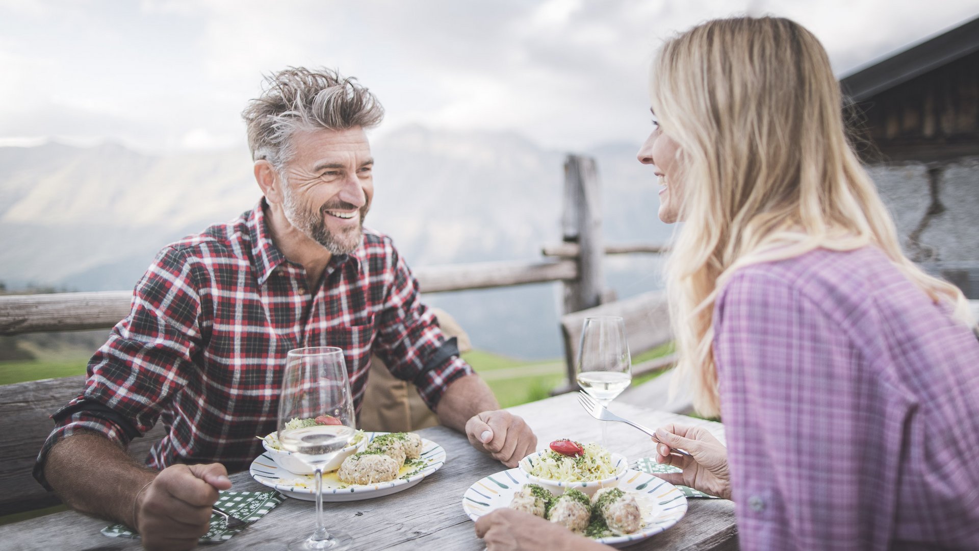 Hiking at Plan de Corones/Kronplatz: unique Couple enjoying meal and wine outdoors at wooden table with mountain view