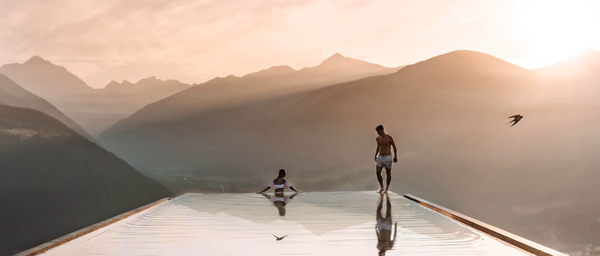 Our Sky Pool in South Tyrol, a rare beauty Two people at an infinity pool overlooking mountains at sunset