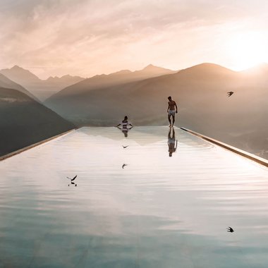 Unser familiengeführtes Hotel in Südtirol Zwei Personen an einem Infinity-Pool mit Bergblick bei Sonnenuntergang