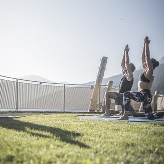 Alpenreych & Hubertus Park Two people practicing yoga outdoors on grass in sunlight