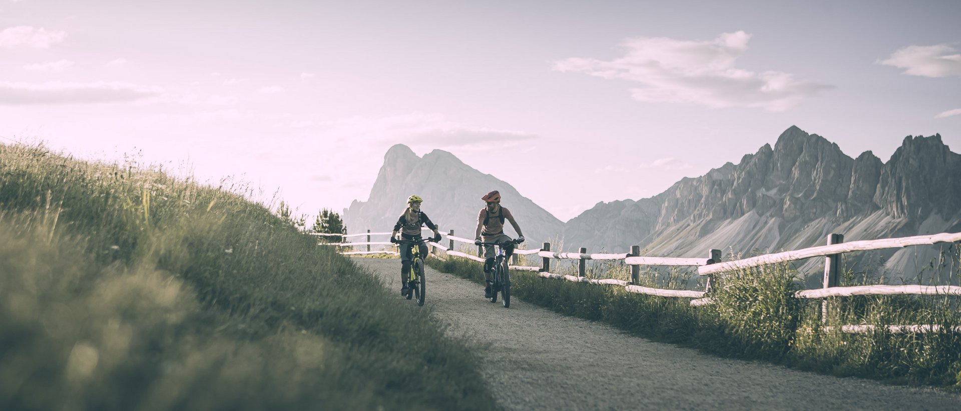 Your 5-star hotel in the Dolomites Two cyclists on a mountain path with fence and mountains in the background