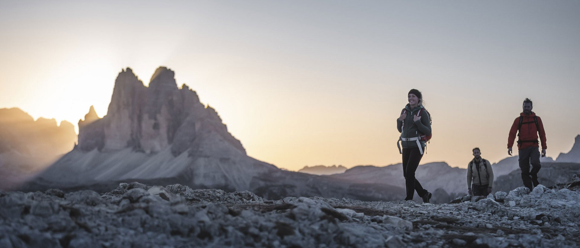 Una vacanza escursionistica da intenditori Tre escursionisti su sentiero roccioso con montagna al tramonto