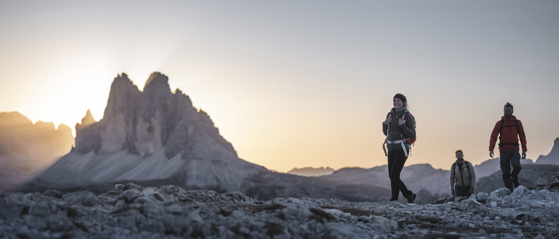 Hiking at Plan de Corones/Kronplatz: unique Three hikers on rocky trail with mountain at sunset