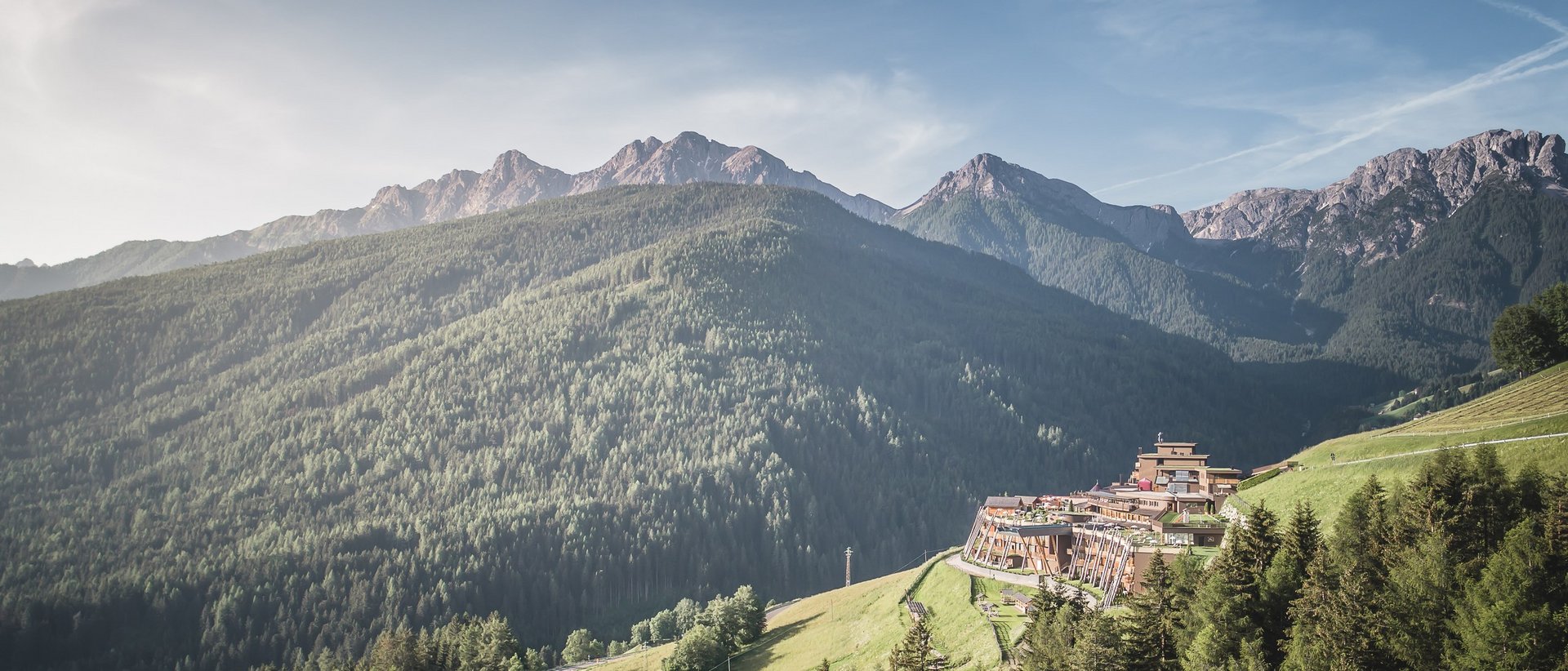 Your 5-star hotel in the Dolomites Mountain landscape with forested hills and a resort on the slope
