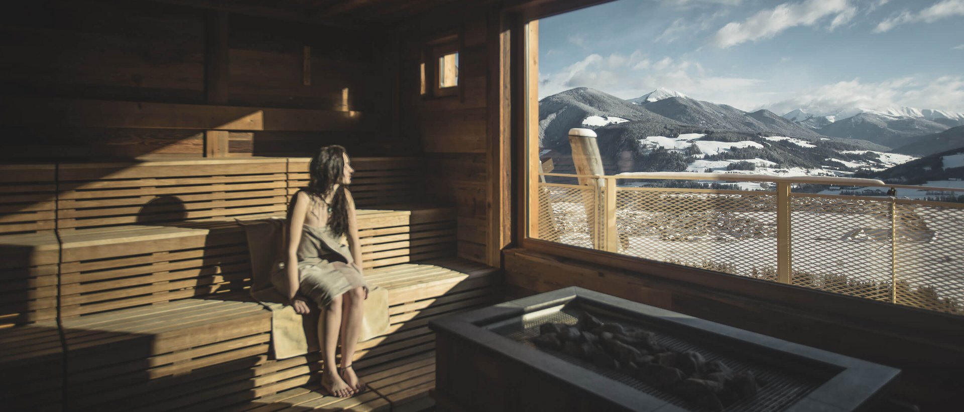 Erholung auf allen Ebenen des Seins Frau in Sauna schaut auf verschneite Berge durch großes Panoramafenster