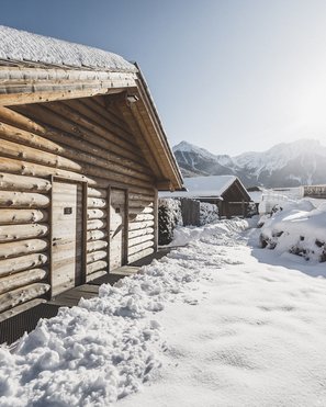 Unsere Parks, Ihre Rückzugsorte Schneebedeckte Holzhütten mit Bergen im Hintergrund bei sonnigem Himmel
