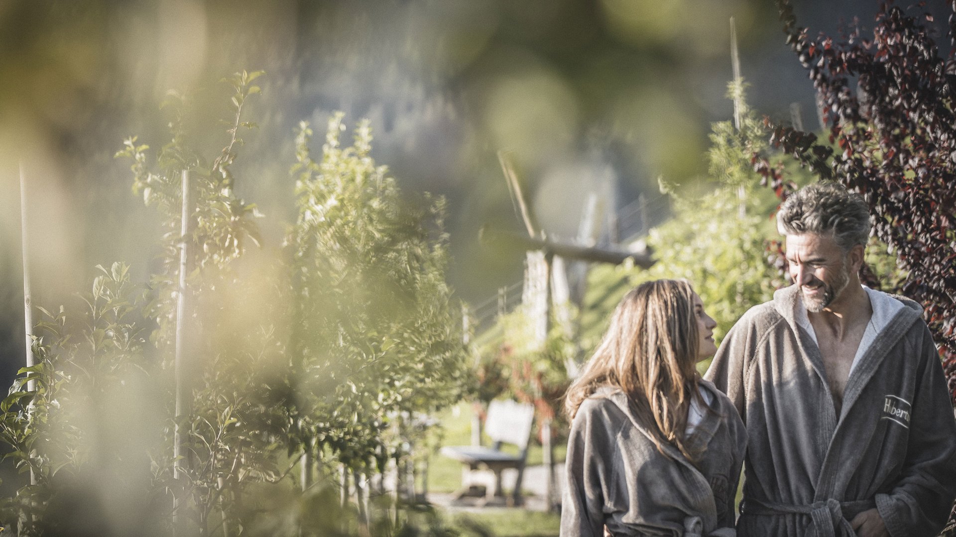Alpenreych & Hubertus Park Couple wearing robes walking outdoors in a garden on a sunny day