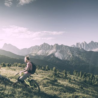 Biking at Plan de Corones/Kronplatz: unique Two mountain bikers resting on a meadow with mountain landscape in the background