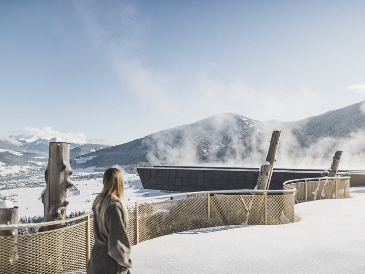 Unsere Parks, Ihre Rückzugsorte Person blickt auf schneebedeckte Berge und dampfende Gebäude bei klarem Himmel