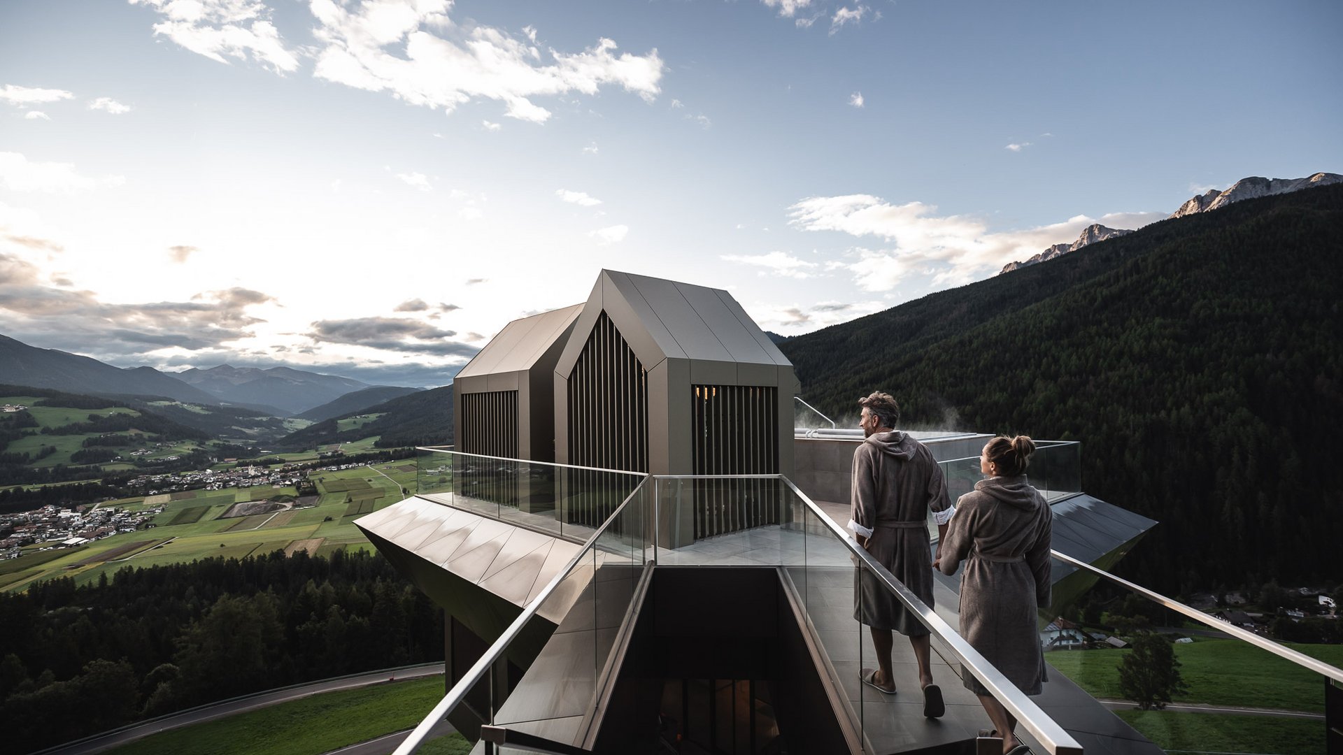 Your 5-star hotel in the Dolomites Couple in robes on rooftop terrace with mountain view and sauna in modern building