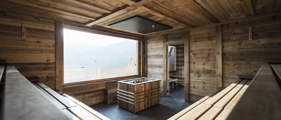 Current news and stories from Olang Modern sauna with wooden walls, benches, and large window with mountain view