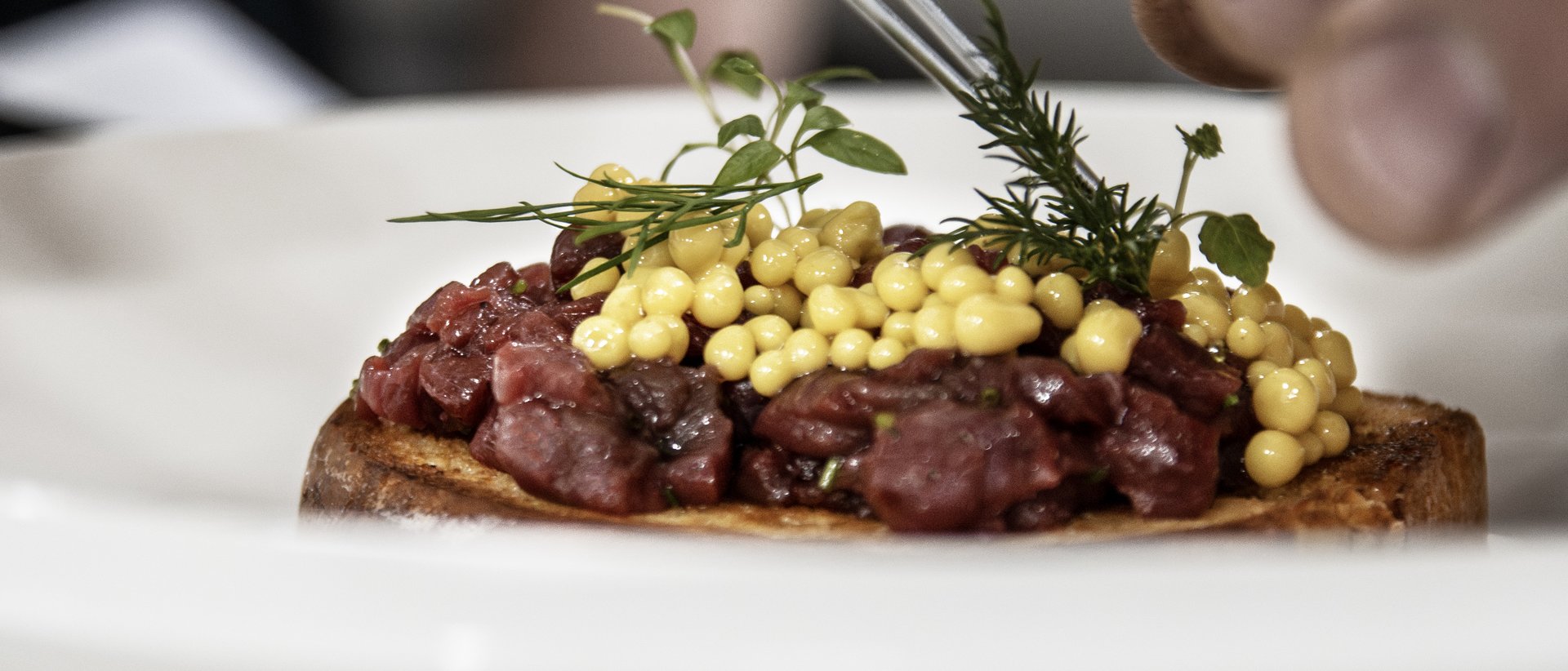 The gourmet hotel in South Tyrol for connoisseurs Hands decorating a dish with fresh herbs and yellow pearls