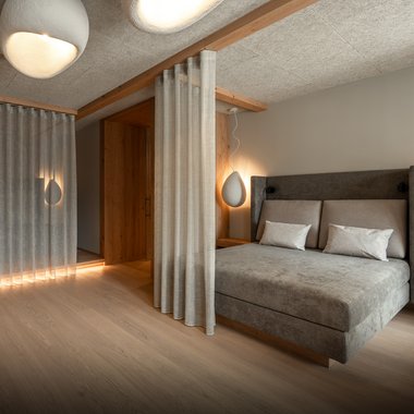 Das Wellnesshotel im Pustertal zum Entspannen Modernes Schlafzimmer mit grauem Bett, Vorhängen und weichen Lampen
