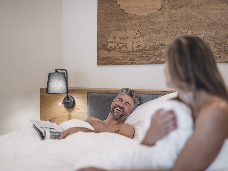 Our 5-star hotel in Italy between heaven and earth Man and woman laughing together in bed under white blanket