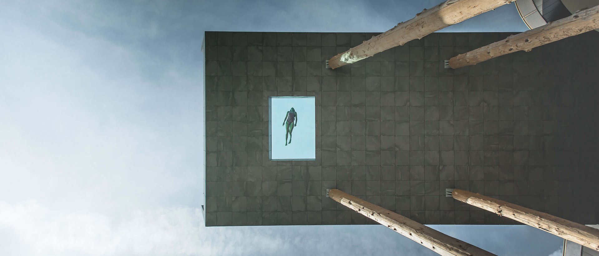 Our Sky Pool in South Tyrol, a rare beauty Swimmer in a glass pool on a high platform against a cloudy sky