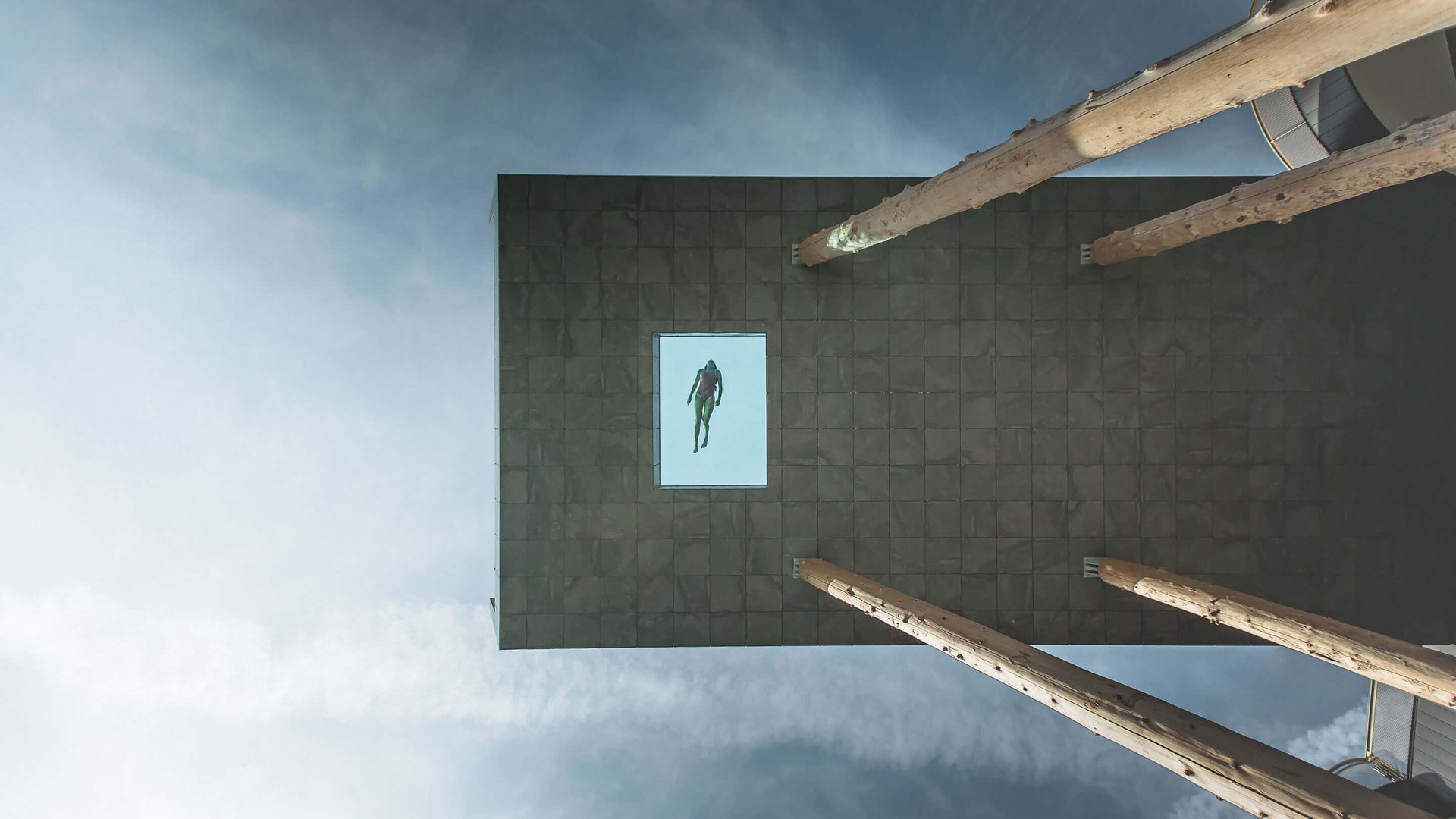 Our hotel vouchers: South Tyrol in gift size Swimmer in a glass pool on a high platform against a cloudy sky