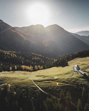 Biking at Plan de Corones/Kronplatz: unique Sunlight over a green alpine meadow with a small house in the mountains