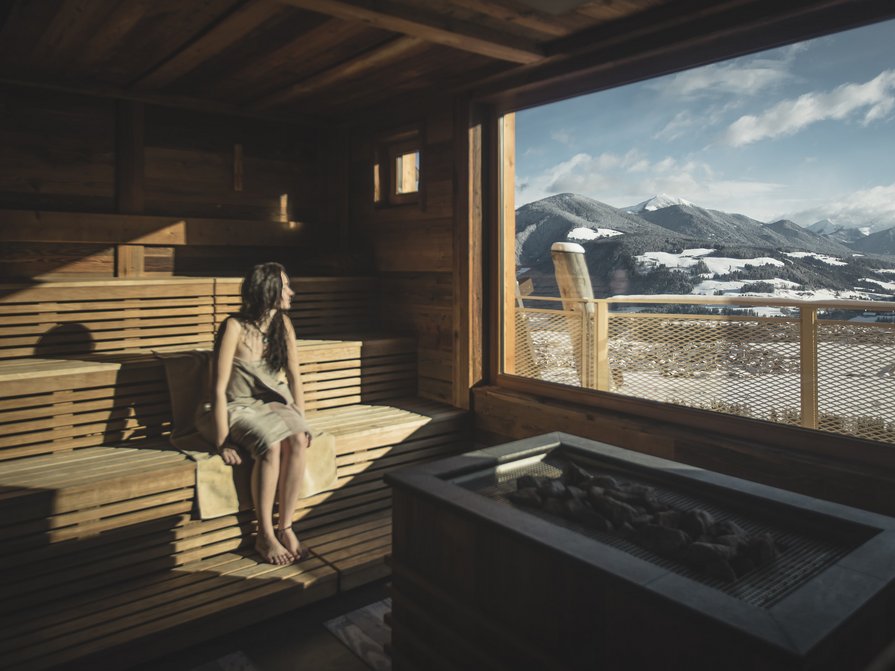 Unser Hotel in Olang zwischen Himmel und Erde Frau sitzt in Sauna mit Blick auf schneebedeckte Berge