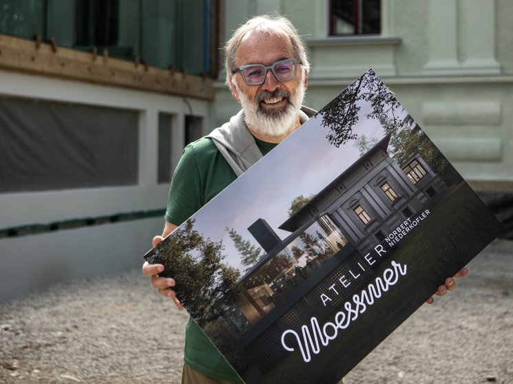 Atelier Moessmer Norbert Niederkofler Man holding a sign with architectural design in front of a historic building