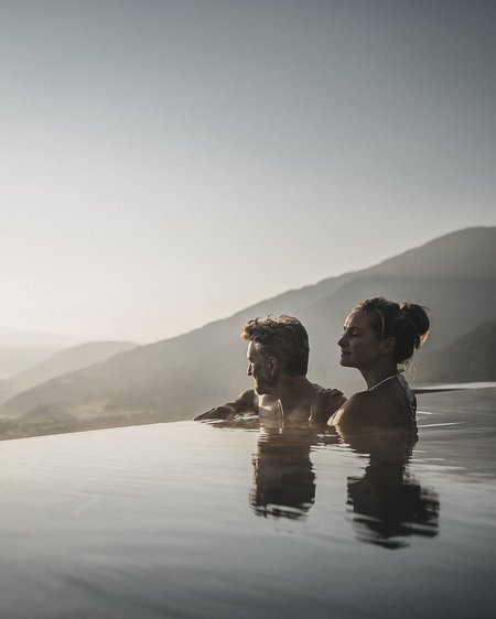 Il nostro attuale catalogo da scaricare Coppia rilassata in piscina a sfioro con vista sulle montagne al tramonto