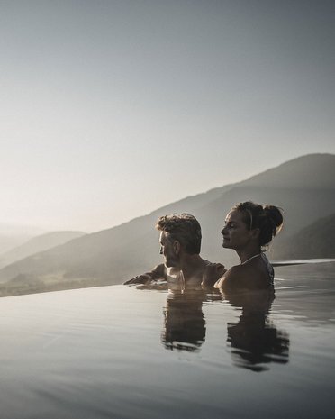Current news and stories from Olang Couple relaxing in infinity pool overlooking mountains at sunset