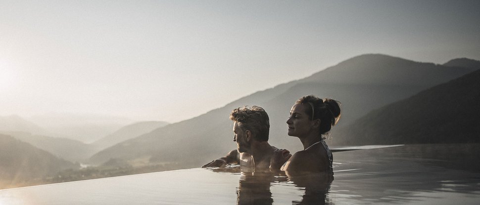 Current news and stories from Olang Couple relaxing in infinity pool overlooking mountains at sunset