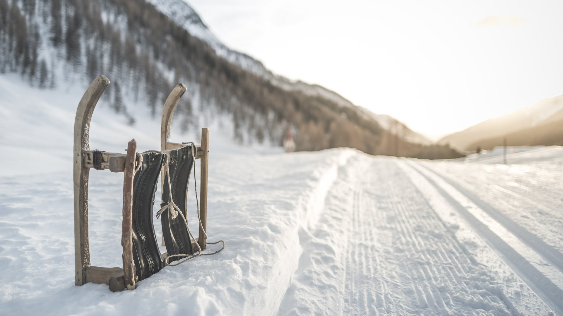 Aktivurlaub in Südtirol: ein Erlebnis Alter Holzschlitten lehnt im Schnee neben einer verschneiten Bergstraße