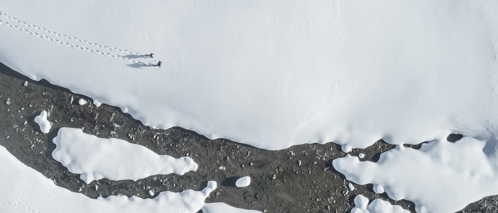 Aktivurlaub in Südtirol: ein Erlebnis Luftaufnahme von zwei Personen, die durch Schnee am Flussufer wandern