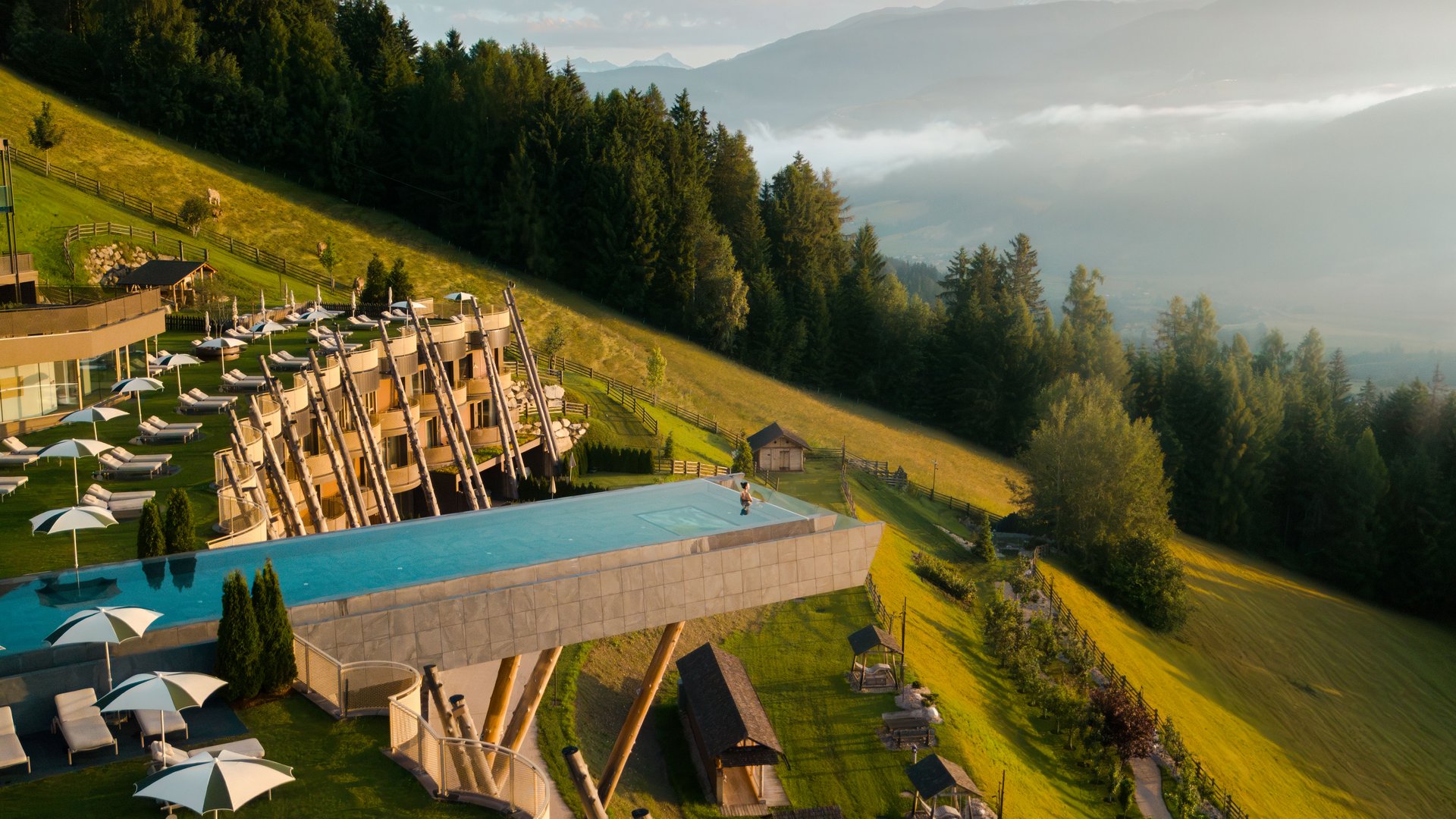 Our 5-star hotel in Italy between heaven and earth Infinity pool on wooden supports on hillside with forest and mountains in background
