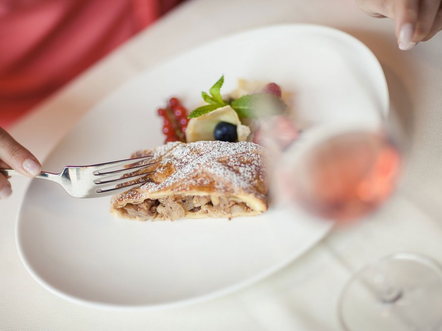 Unser Hotel in Olang zwischen Himmel und Erde Person schneidet Apfelstrudel mit Beeren auf einem weißen Teller
