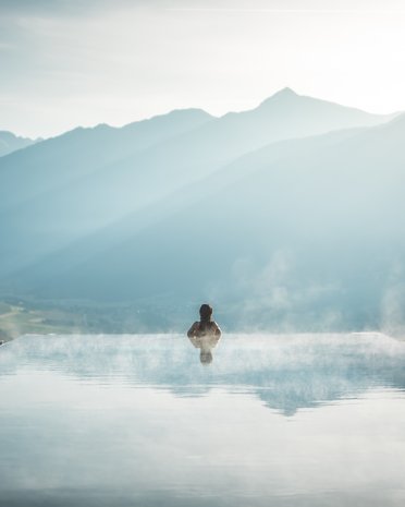 Current news and stories from Olang Person in steaming infinity pool overlooking misty mountain landscape