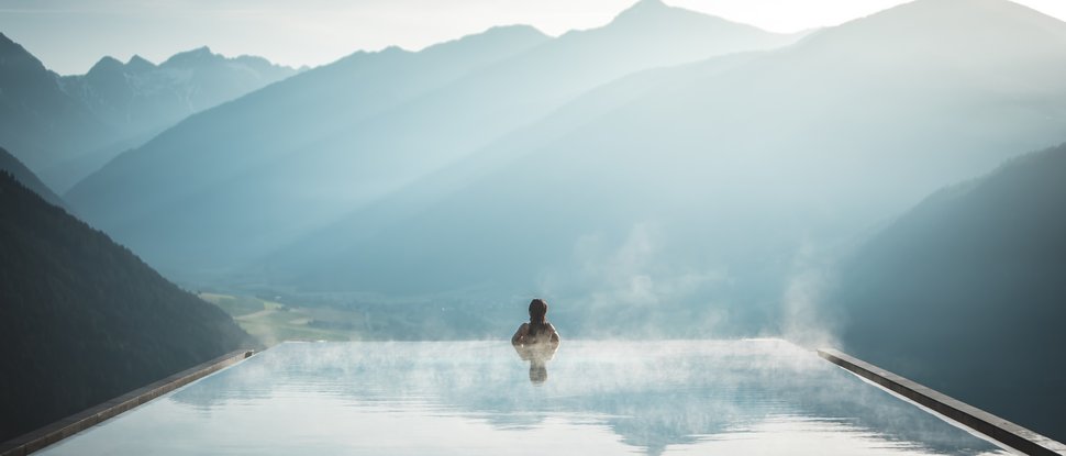 Our 5-star hotel in Italy between heaven and earth Person in steaming infinity pool overlooking misty mountain landscape