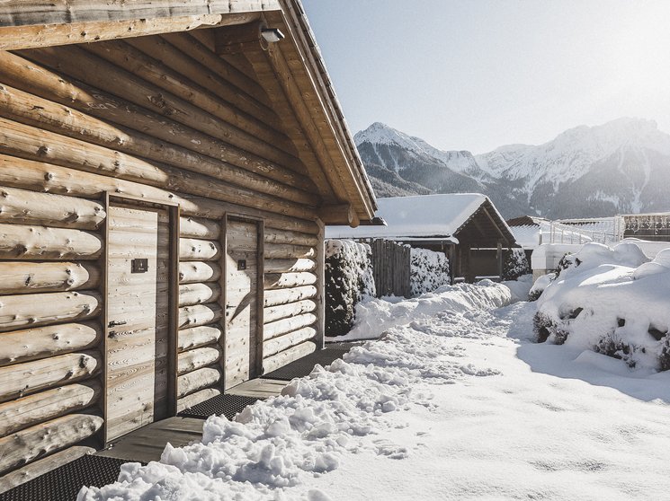 Our wellness hotel in Val Pusteria for relaxation seekers Wooden cabin with snow-covered roof in snowy mountain landscape under sunlight