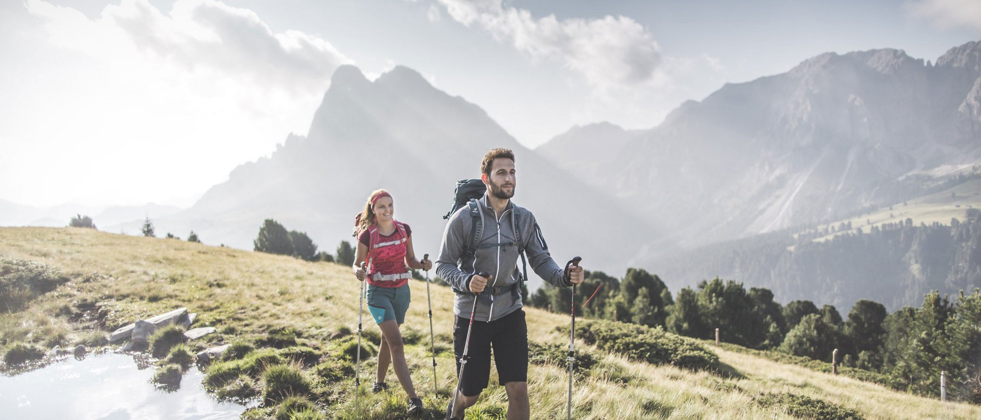 Una vacanza escursionistica da intenditori Due escursionisti con zaini e bastoncini su prato di montagna al sole