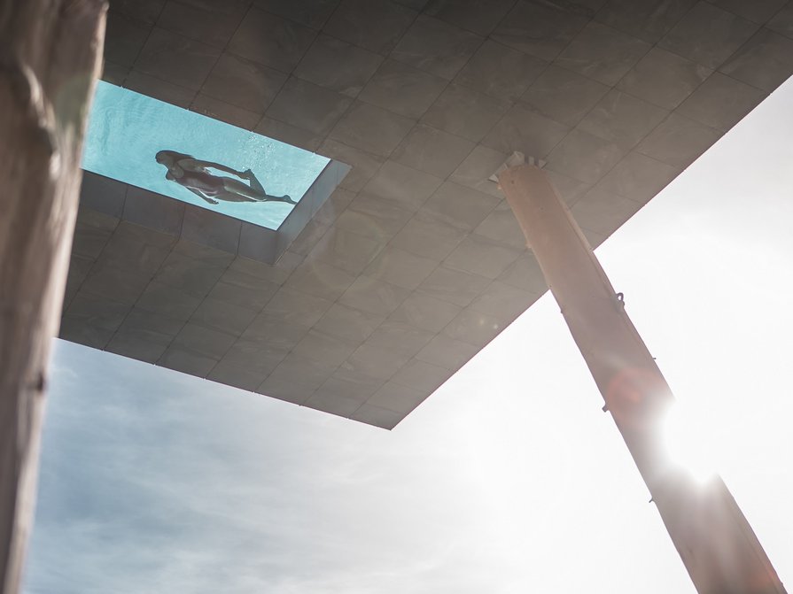 Our 5-star hotel in Italy between heaven and earth Woman swimming in a glass-bottom pool above a building