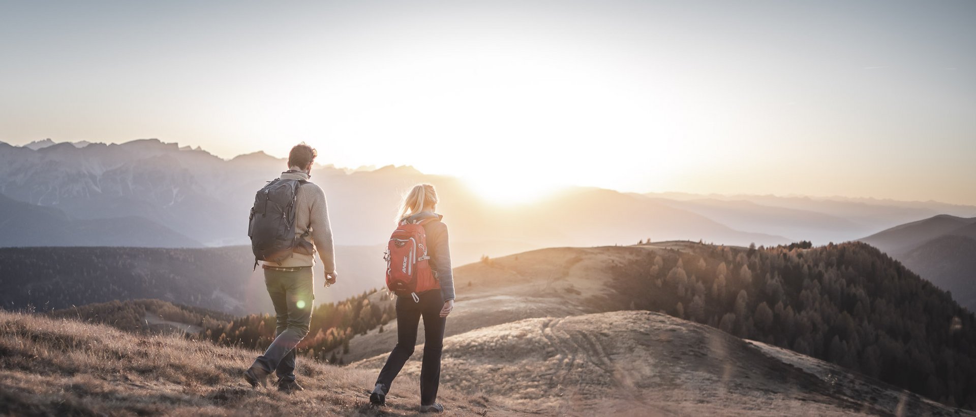 Active holidays in South Tyrol: a great experience Two hikers with backpacks walking at sunset in the mountains
