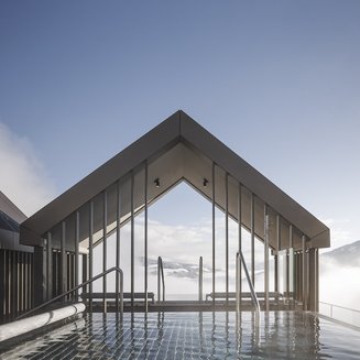 Our wellness hotel in Val Pusteria for relaxation seekers Infinity pool with mountain view and modern canopy under clear sky