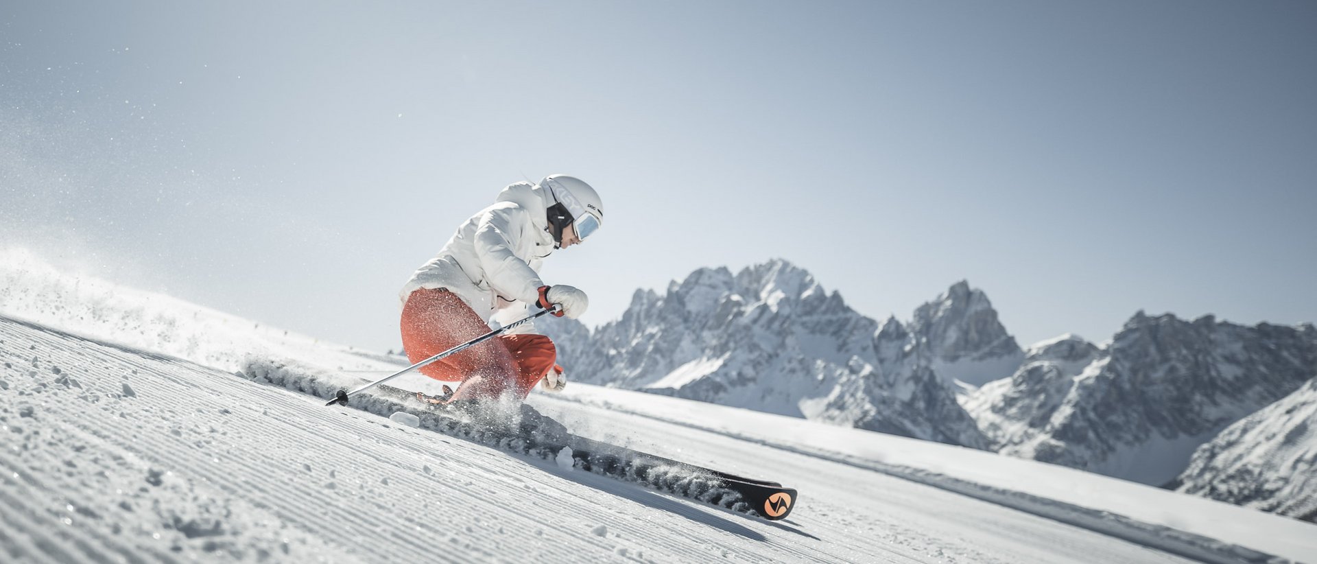 Aktivurlaub in Südtirol: ein Erlebnis Skifahrer fährt auf präparierter Piste vor Bergkulisse bei strahlendem Himmel