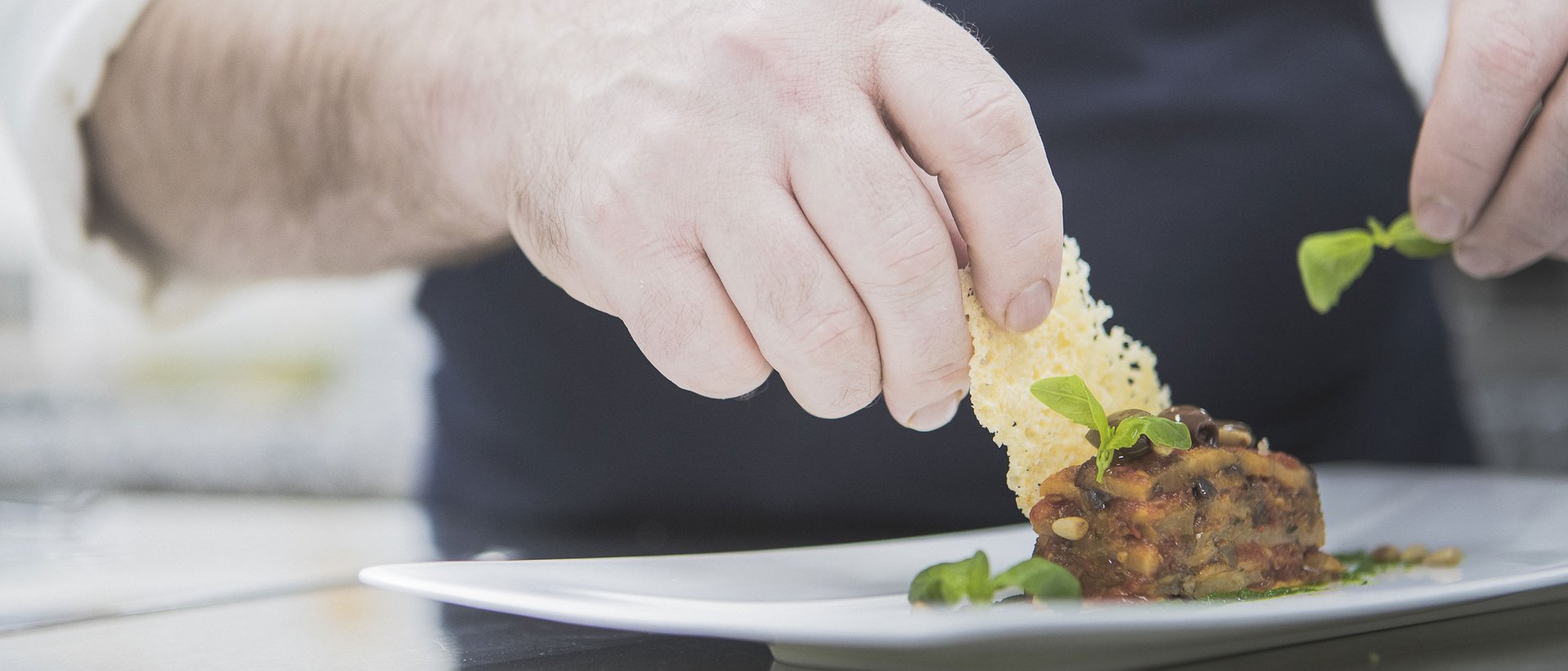 The gourmet hotel in South Tyrol for connoisseurs Chef garnishing gourmet dish with cheese crisp and fresh herbs