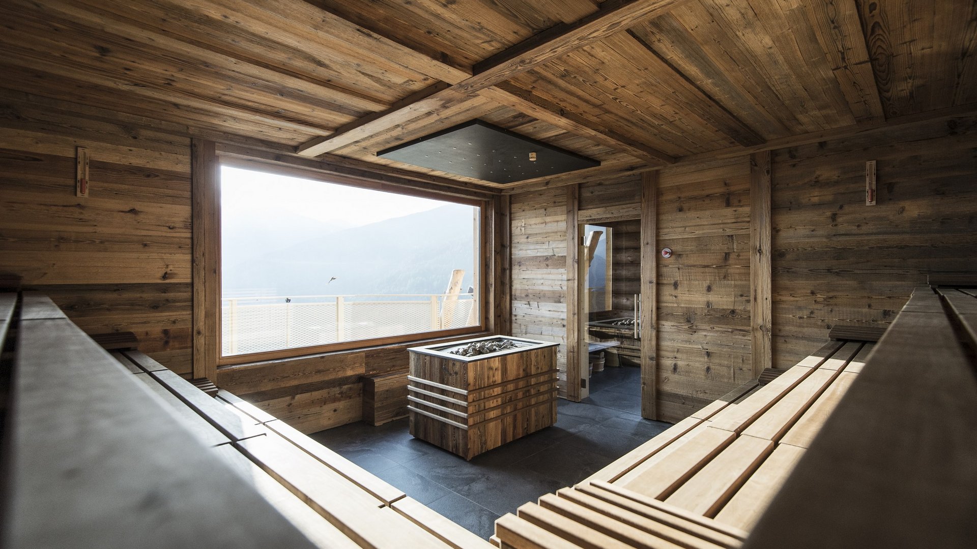 Our wellness hotel in Val Pusteria for relaxation seekers Sauna room with wooden interior and large window overlooking mountains