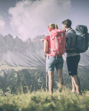 Bruneck: shopping & more Hikers with backpacks looking at forested mountains under cloudy sky