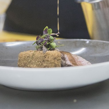 A place to enjoy Elegant plated dish with sauce being poured over breaded meat and herbs