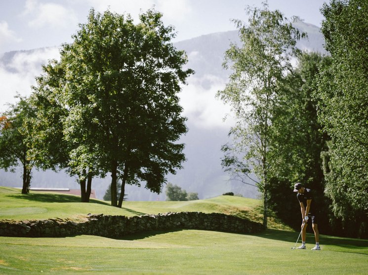 Golfclub Pustertal - Your golf course at Mt. Kronplatz Person playing golf on green course with trees and mountains in background