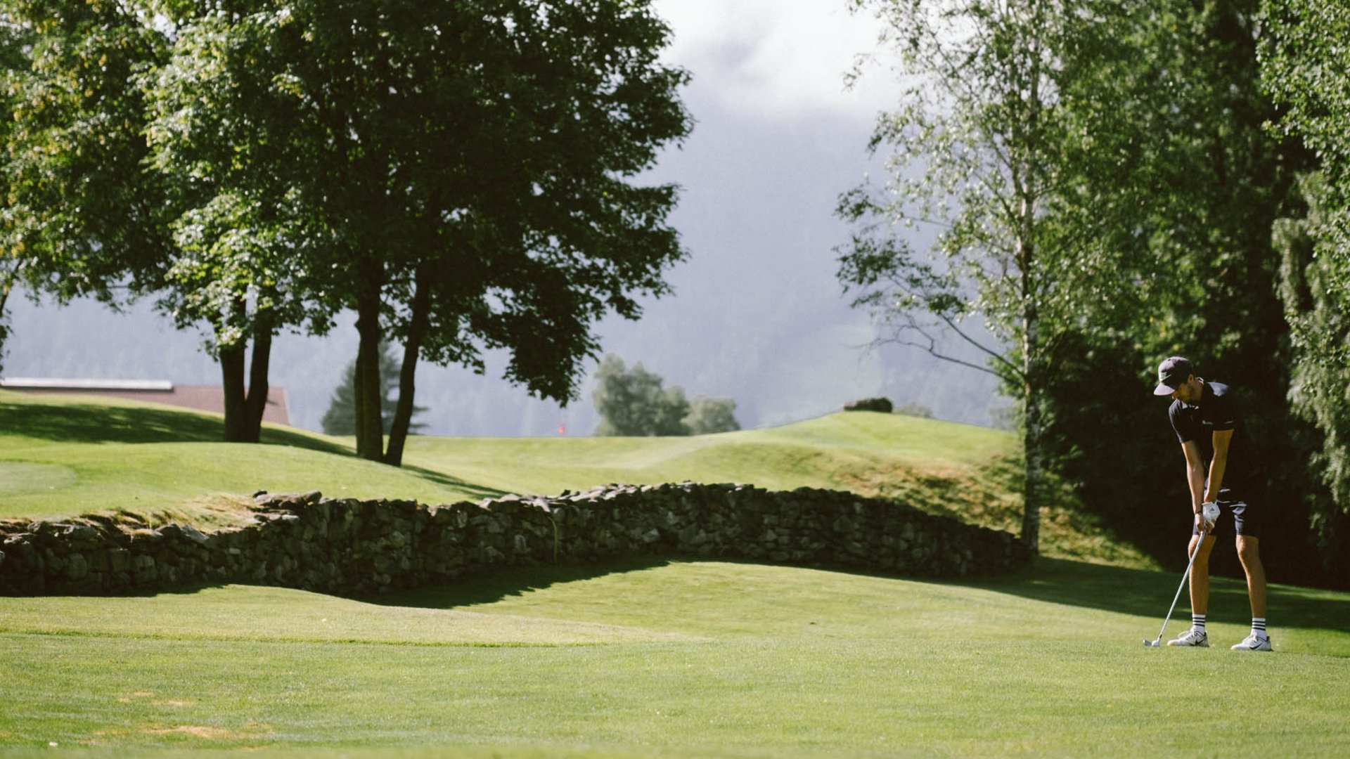 Golfclub Pustertal - Your golf course at Mt. Kronplatz Person playing golf on green course with trees and mountains in background