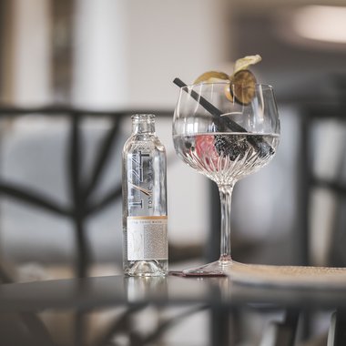 A place to enjoy Tonic water bottle next to cocktail glass with berries and lime slice